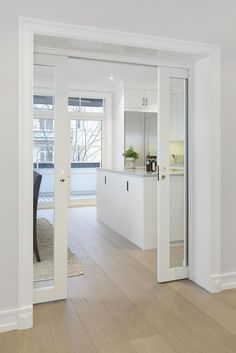 an empty living room with white walls and hardwood floors is seen from the doorway to the dining area