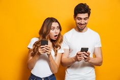 two people standing next to each other looking at their cell phones and making funny faces