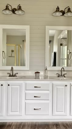 a bathroom with two sinks, mirrors and lights on the wall above them is shown