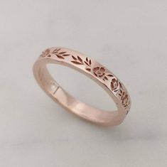 a rose gold wedding ring with leaves and flowers engraved on the side, set against a plain white background