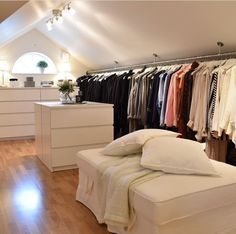 a bedroom with a bed, dresser and clothes on hangers in front of it