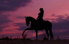 a woman riding on the back of a brown horse at sunset with clouds in the background