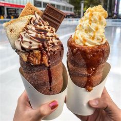 two ice cream sundaes in paper cups with chocolate and whipped cream on top