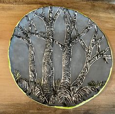 a metal plate with trees on it sitting on top of a wooden table next to a wall