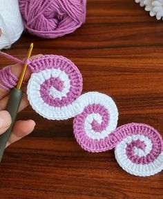 someone crocheting circles with yarn on a wooden table next to balls of yarn