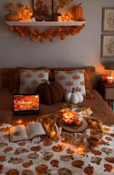 a bed topped with lots of pumpkins and candles next to an open laptop computer