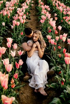 a man and woman sitting in the middle of a field full of pink tulips