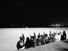 black and white photograph of people sitting on the beach with their arms in the air