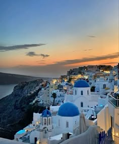 the sun is setting over some white buildings with blue domes on them and water in the background