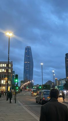 a city street filled with lots of traffic next to tall buildings at night, and people walking on the sidewalk