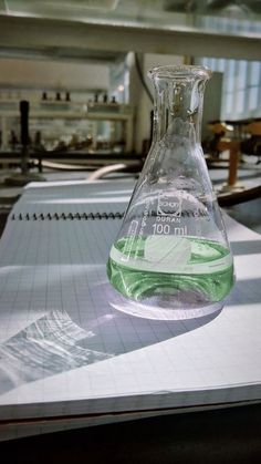 a flask filled with purple liquid sitting on top of a white table next to a piece of paper