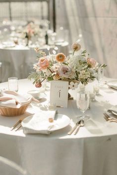 the table is set with white linens and silverware, flowers in vases