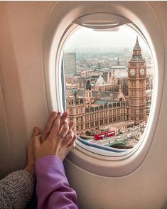 a person's hand on the window of an airplane with big ben in the background