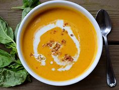 a bowl of carrot soup with spinach leaves on the side and spoons next to it