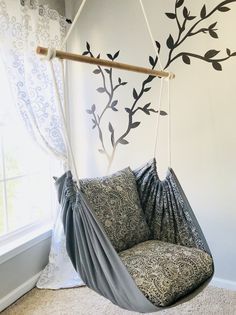 a swing chair hanging in front of a window with curtains on both sides and a tree branch painted on the wall behind it