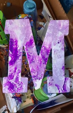 the letter m is made out of purple and white marbled paper with water droplets on it