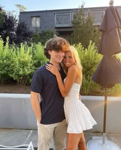 a man and woman standing next to each other in front of an umbrella covered patio