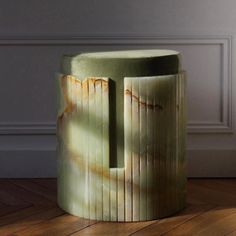 a green stool sitting on top of a hard wood floor next to a white wall