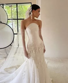 a woman in a white wedding dress standing next to a window with her hands on her hips