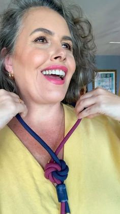 a woman with gray hair wearing a yellow shirt and blue tie is smiling at the camera