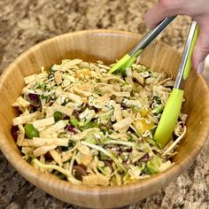 a person holding two chopsticks over a salad in a wooden bowl on top of a counter