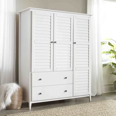 a white armoire sitting next to a window in a room with a rug on the floor