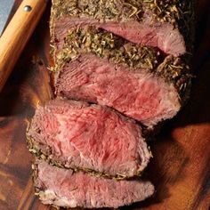 sliced roast beef with herbs and seasoning on a cutting board next to a knife