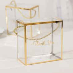 two clear boxes with the words thank you in gold lettering on them, sitting on a white surface