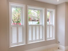 three windows with white wooden shutters in a home's living room, one is empty