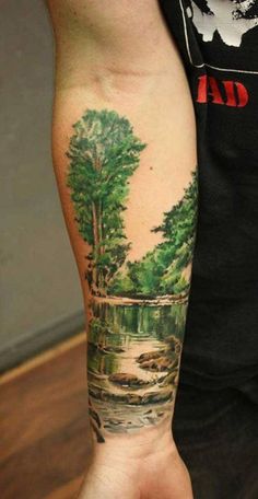 a man's arm with a painting on it that has trees and water in it