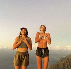 two women standing on top of a mountain next to each other with their hands together