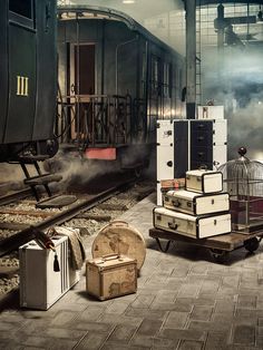 suitcases and boxes are sitting on the ground next to a train in an industrial building