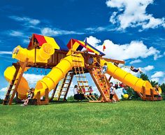 children playing on a giant yellow slide in the grass with blue sky and clouds behind them