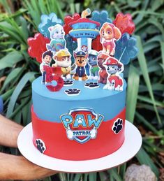 a paw patrol themed cake is being held up by someone's hand in front of some plants