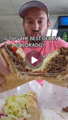 a man is holding up a sandwich with meat and lettuce on it in front of him