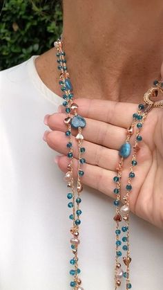 a woman wearing a long necklace with blue beads and gold chains on her hands,