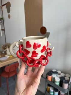 a hand holding up a cup with hearts painted on it and chains attached to the handle