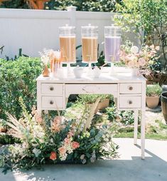 a white table topped with lots of flowers and glasses filled with liquid on top of it