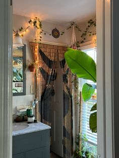 an open door leading to a bathroom with plants on the wall and curtains hanging from the ceiling