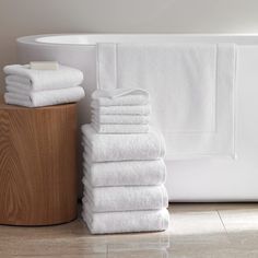 a stack of white towels sitting on top of a wooden block next to a bath tub