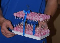 a man holding a tray with pink donuts on it and toothpicks sticking out of them