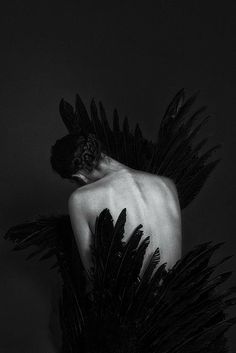 a black and white photo of a naked man with feathers on his back, in the dark