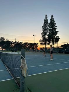 two people are playing tennis on the court at sunset or dawn with their rackets in hand