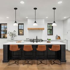 a large kitchen with an island and bar stools next to it, along with three lights hanging from the ceiling