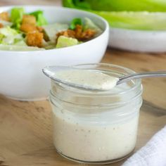 a bowl of salad with dressing next to it on a cutting board and another bowl of salad in the background