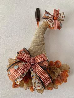 a bird made out of fabric and ribbon on a white wall with a spoon in it's mouth