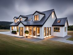 a large white house with black roof and lights on it's windows at night