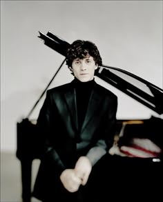 a man in a black suit sitting at a piano