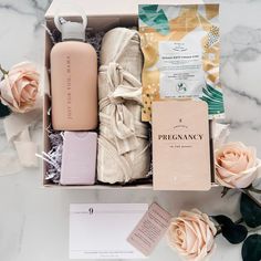 an open box filled with personal care items next to pink flowers and cards on a marble surface