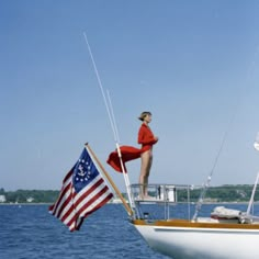 a woman standing on the bow of a sailboat with an american flag flying from it